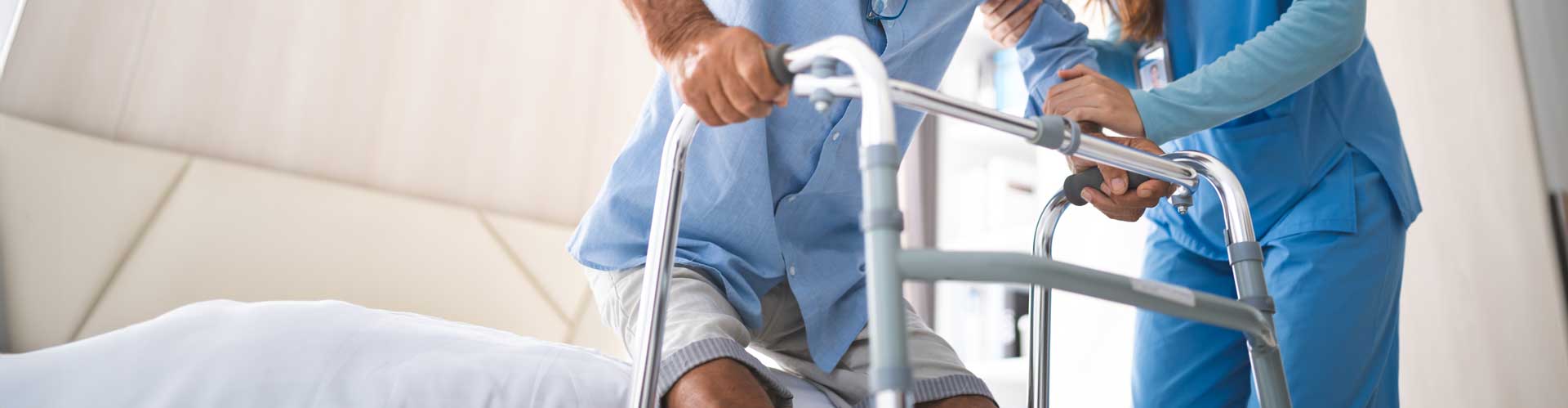 Pflegebedürftiger stützt sich auf Gehhilfe, Pflegefachfrau unterstützt in